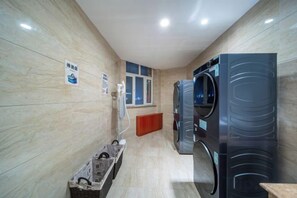 Un cuarto de lavandería con dos lavadoras grandes, una secadora y un pequeño cubo de basura.