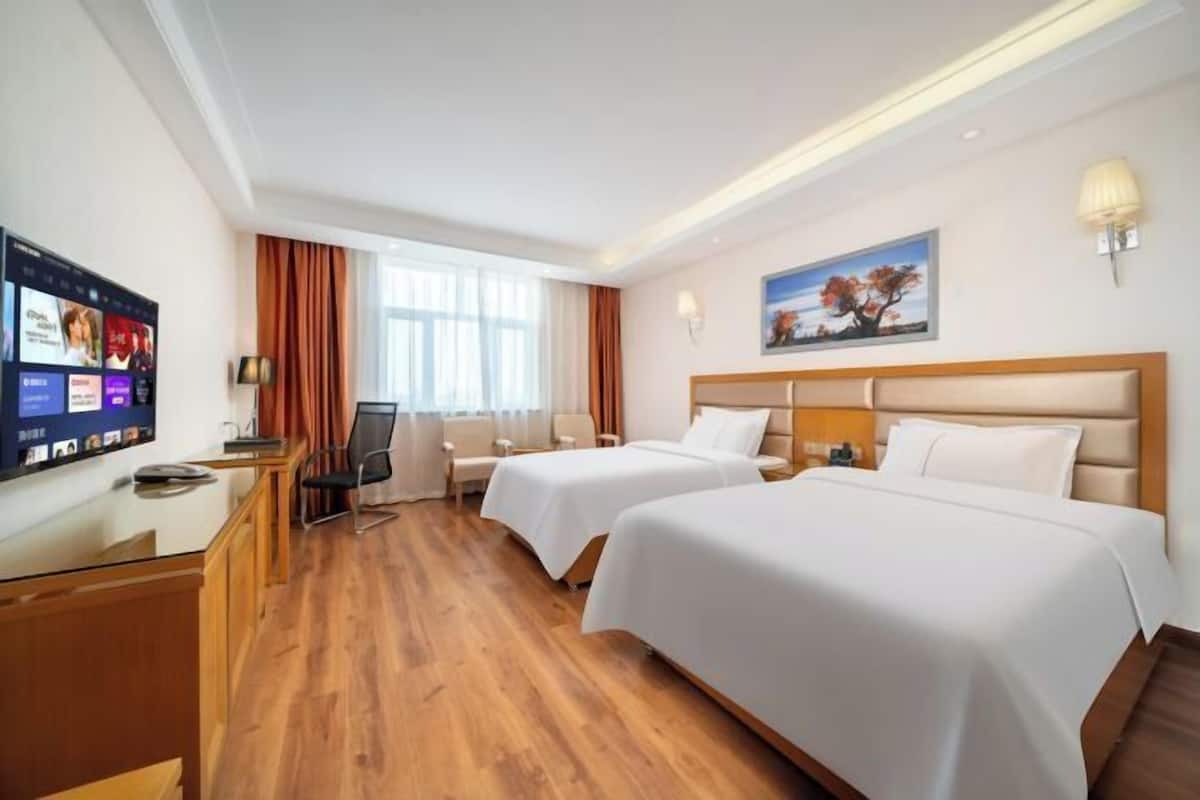 Habitación de hotel con dos camas, un escritorio, un televisor y un cuadro en la pared.