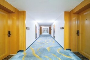A hotel corridor with wooden doors on both sides, a carpeted floor, and a long hallway leading to a distant door. - Boyu Hotel (Karamay)