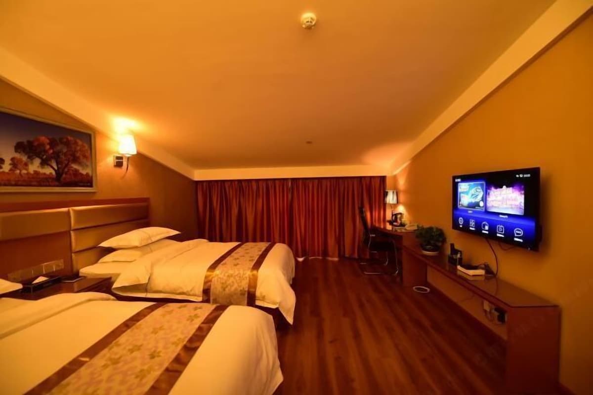 A hotel room with two beds, a TV on the wall, a desk with a lamp, and a painting on the wall.