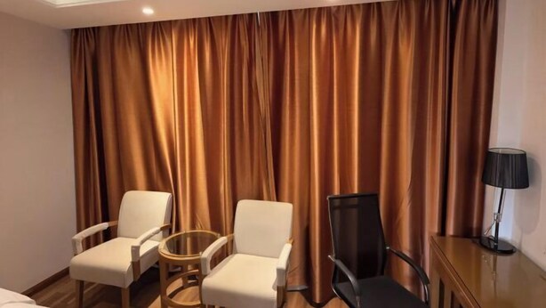 Ein Hotelzimmer mit einem Bett, zwei weißen Sesseln, einem runden Tisch, einem schwarzen Stuhl und einer Lampe.