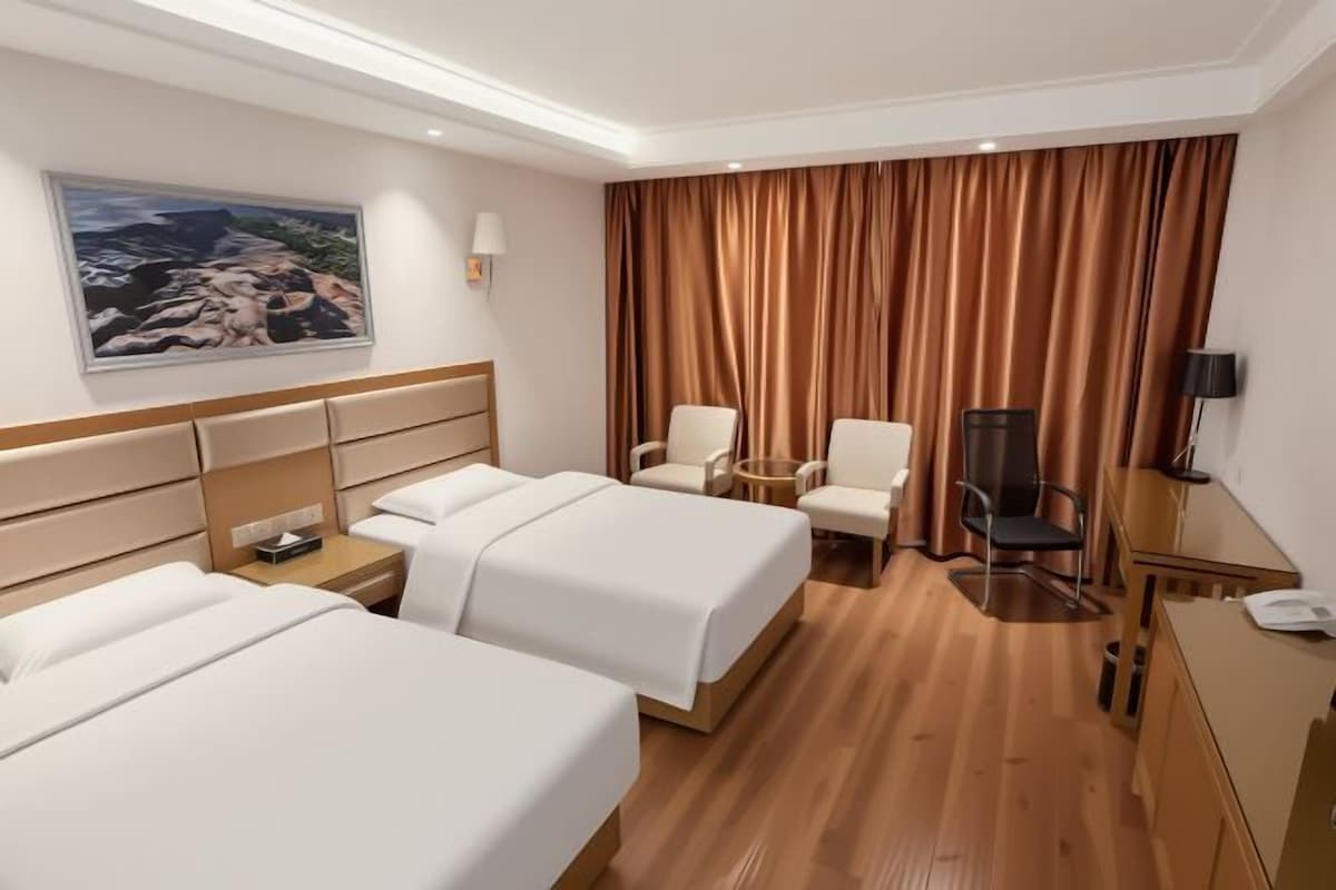 A hotel room with two beds, a desk, a chair, a TV, and a painting on the wall.