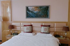 A hotel room with a large bed, two bedside tables, a headboard, and a painting on the wall. - Boyu Hotel (Karamay)