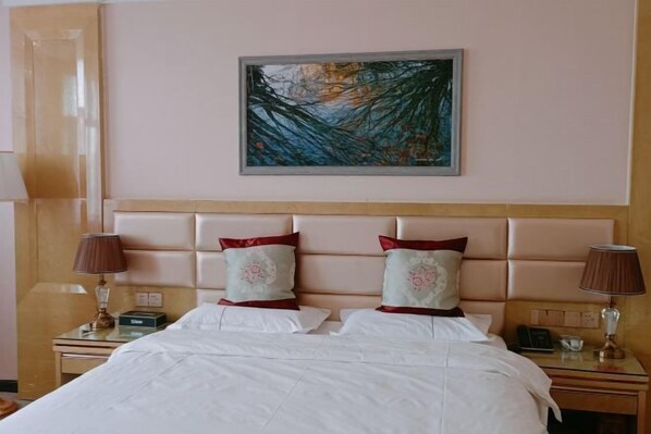 Una habitación de hotel con una cama grande, dos mesitas de noche, un cabecero y un cuadro en la pared.