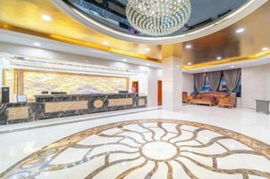 Um hall de hotel com uma recepção de mármore, um candelabro e um piso estampado.