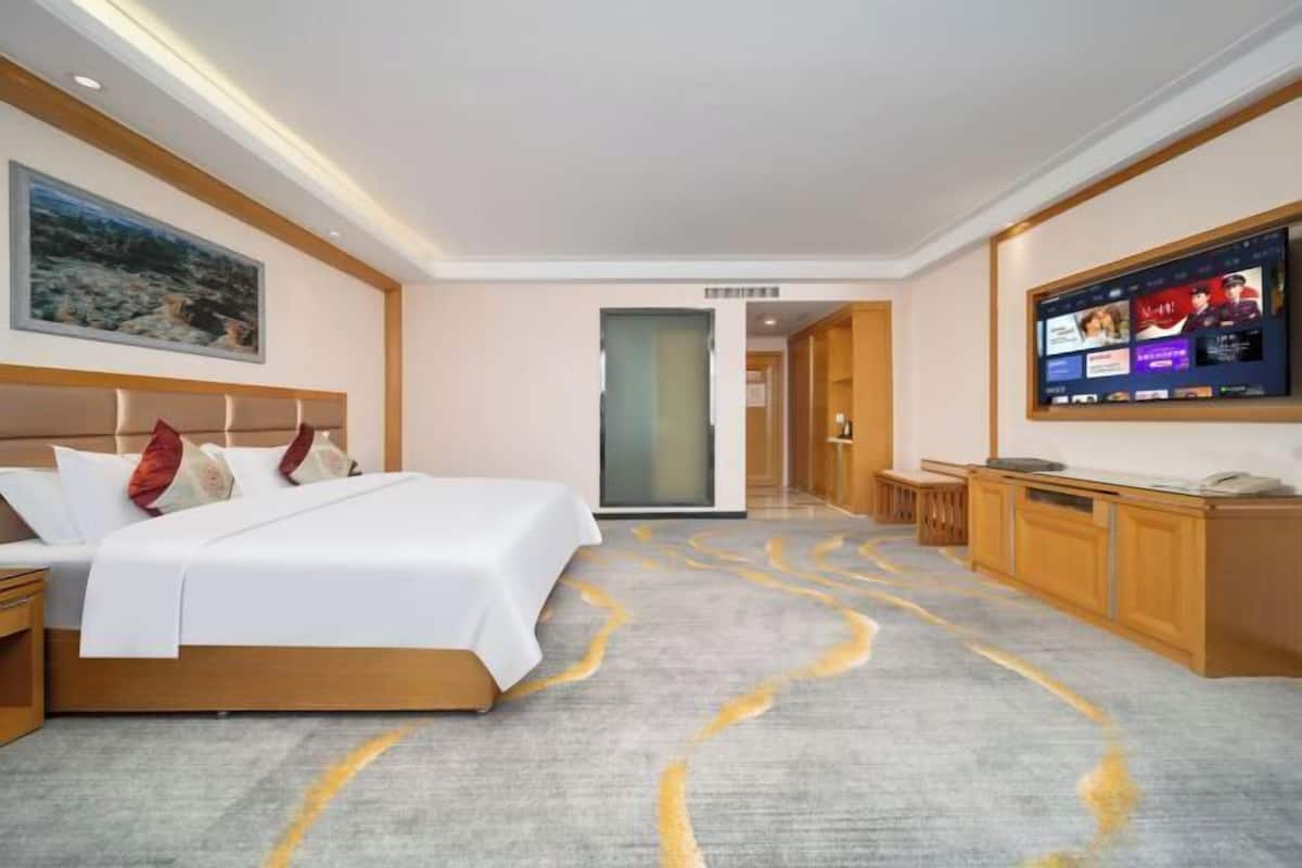 Una habitación de hotel con cama, televisión, escritorio y un cuadro en la pared.