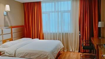 Ein Hotelzimmer mit zwei Betten, einem Schreibtisch, einem Stuhl und einem großen Fenster mit Vorhängen.