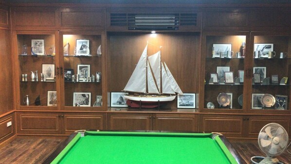 A billiards table in a room with wooden paneling, a model sailboat, and shelves with framed pictures and decorative items. - Treehouse and swimming pool (Mae Chan)