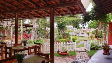 Un espacio de patio cubierto con una mesa y sillas de madera, rodeado de macetas con plantas y una valla de piquetes blanca.