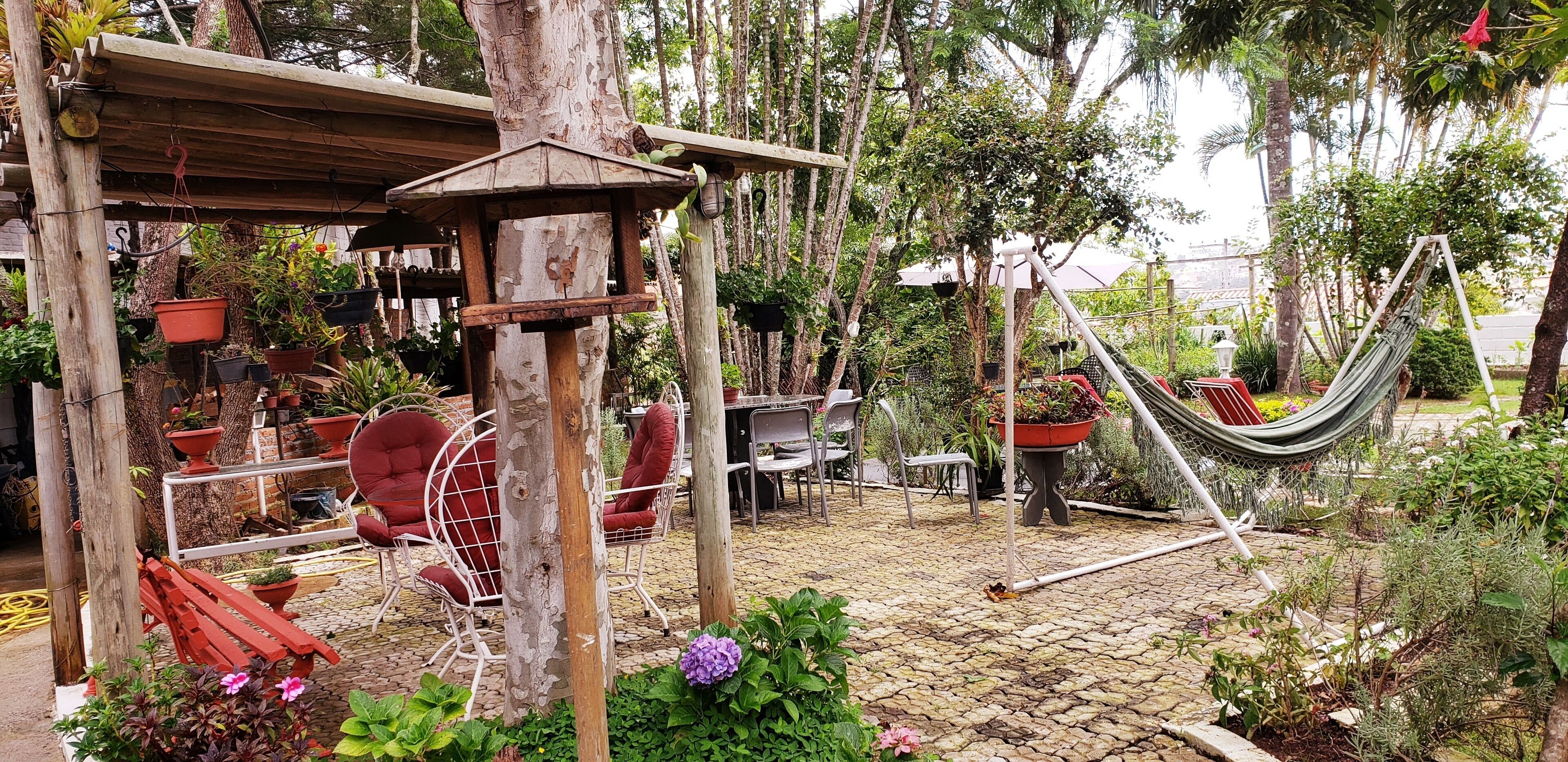 Um pátio com jardim, mobiliário de exterior, uma rede e plantas em vasos.
