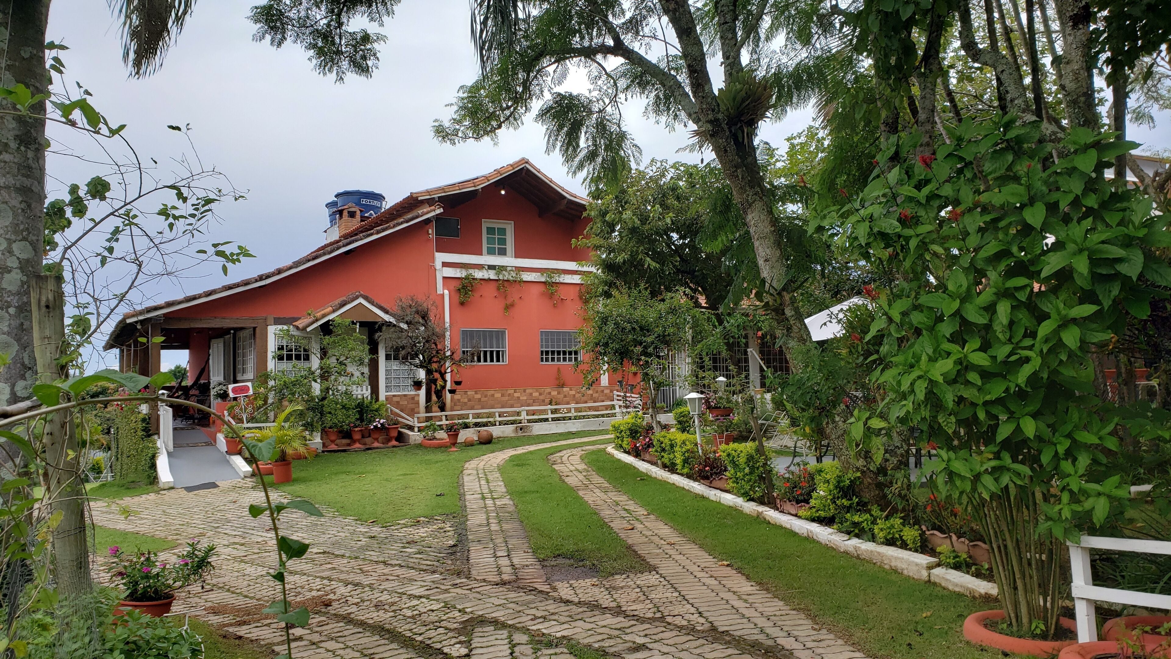 A red house with a garden, paved pathway, and a water tank.