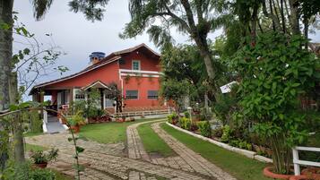 A red house with a garden, paved pathway, and a water tank.