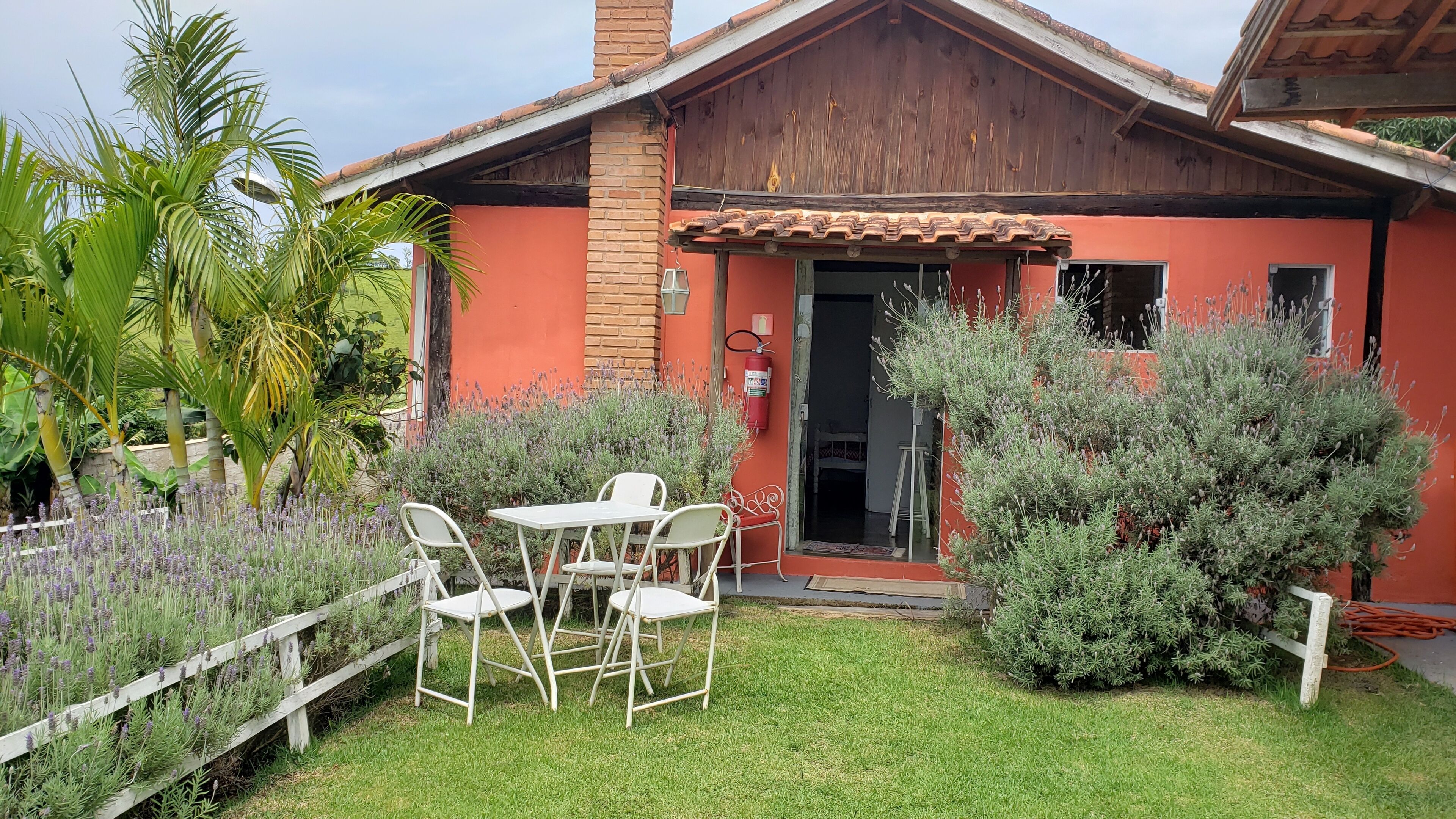 Una pequeña casa con fachada roja, techo de tejas y un pequeño patio con mesa y sillas.
