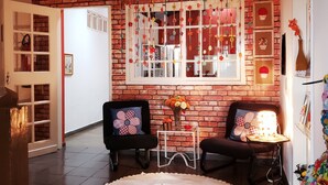 A cozy room with a brick wall, two black armchairs, a small table with a vase of flowers, and a large window with decorative elements. - Pousada Calu (Cunha)