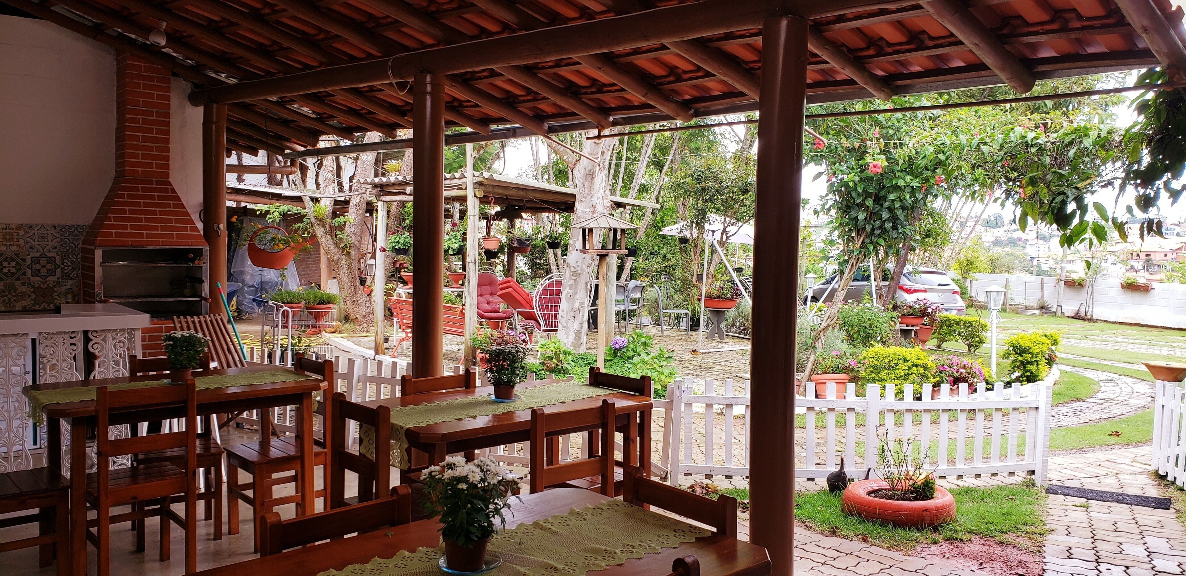 An outdoor patio with wooden tables and chairs, a brick oven, and potted plants.