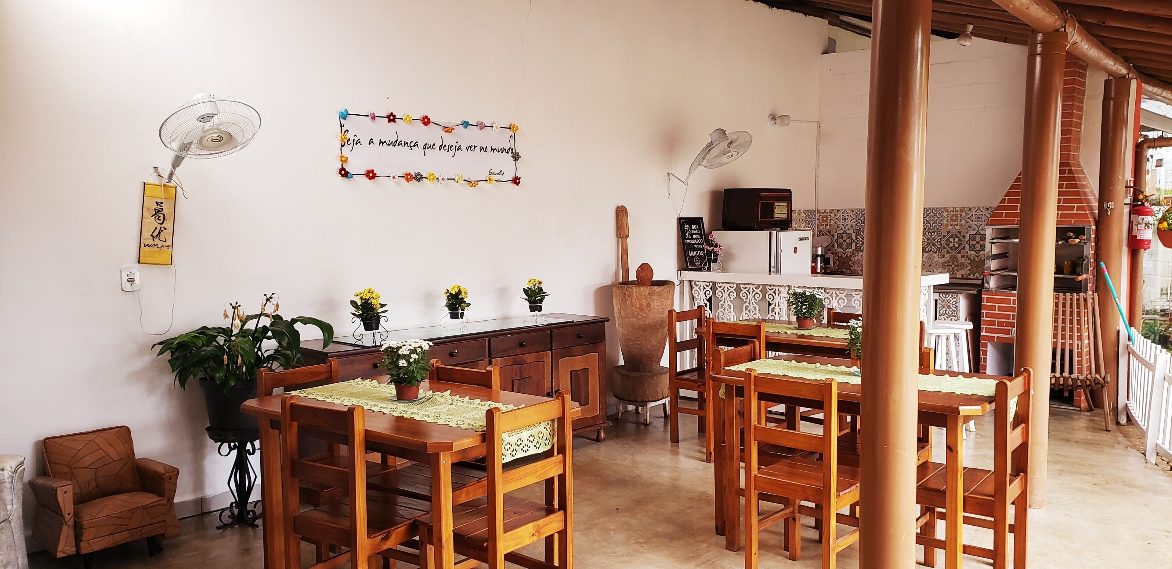 A cozy dining area with wooden tables and chairs, a kitchen area with a brick oven, and decorative plants.