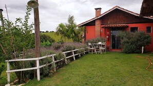 A red house with a wooden fence, a grassy lawn, and a garden with purple flowers. - Pousada Calu (Cunha)