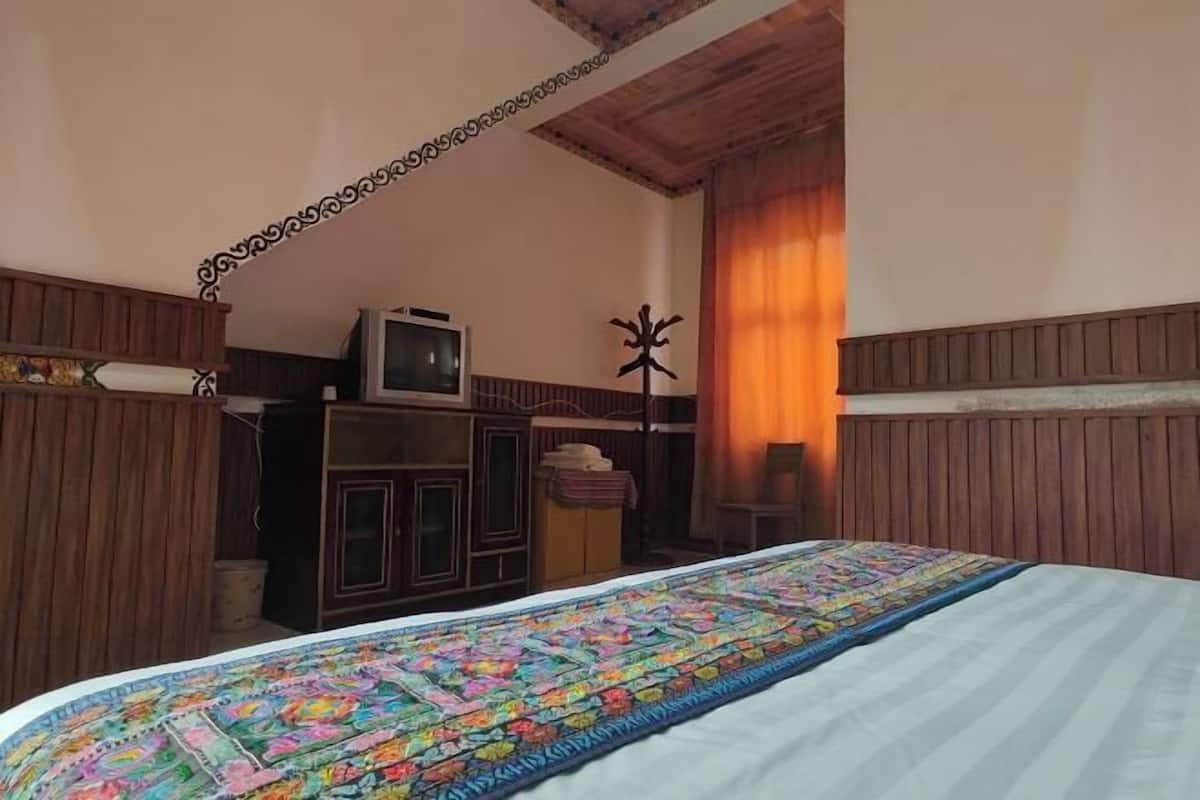 Une chambre à coucher comprenant un lit, une armoire en bois, un téléviseur posé sur un meuble et un élément décoratif mural.