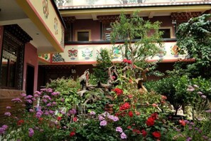 Un edificio tradicional con un patio, un árbol pequeño y flores coloridas.