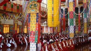 Ein großer Saal mit Reihen sitzender Personen, möglicherweise Mönche, in einem traditionellen Ambiente mit aufwendiger Dekoration.