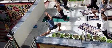 A group of people performing yoga on outdoor mats with a decorative wall and plants in the background.