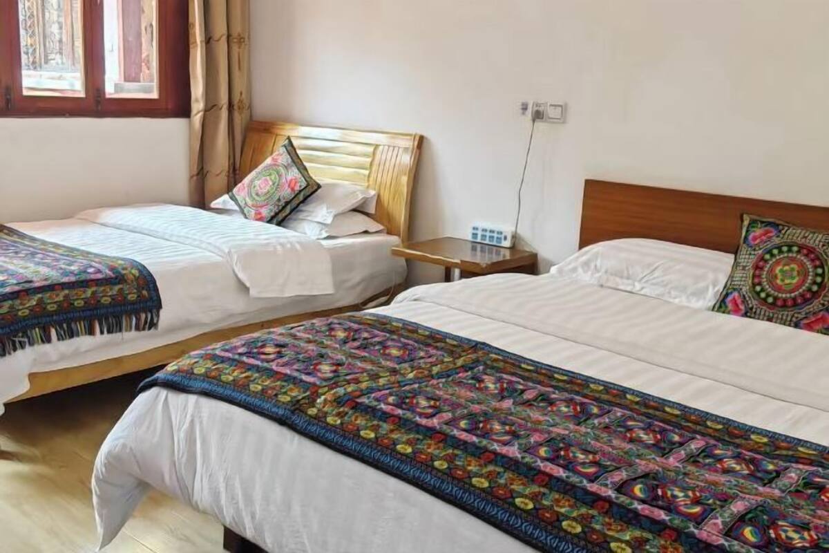 Deux lits simples avec des têtes de lit en bois, du linge de lit blanc et des couvertures colorées.