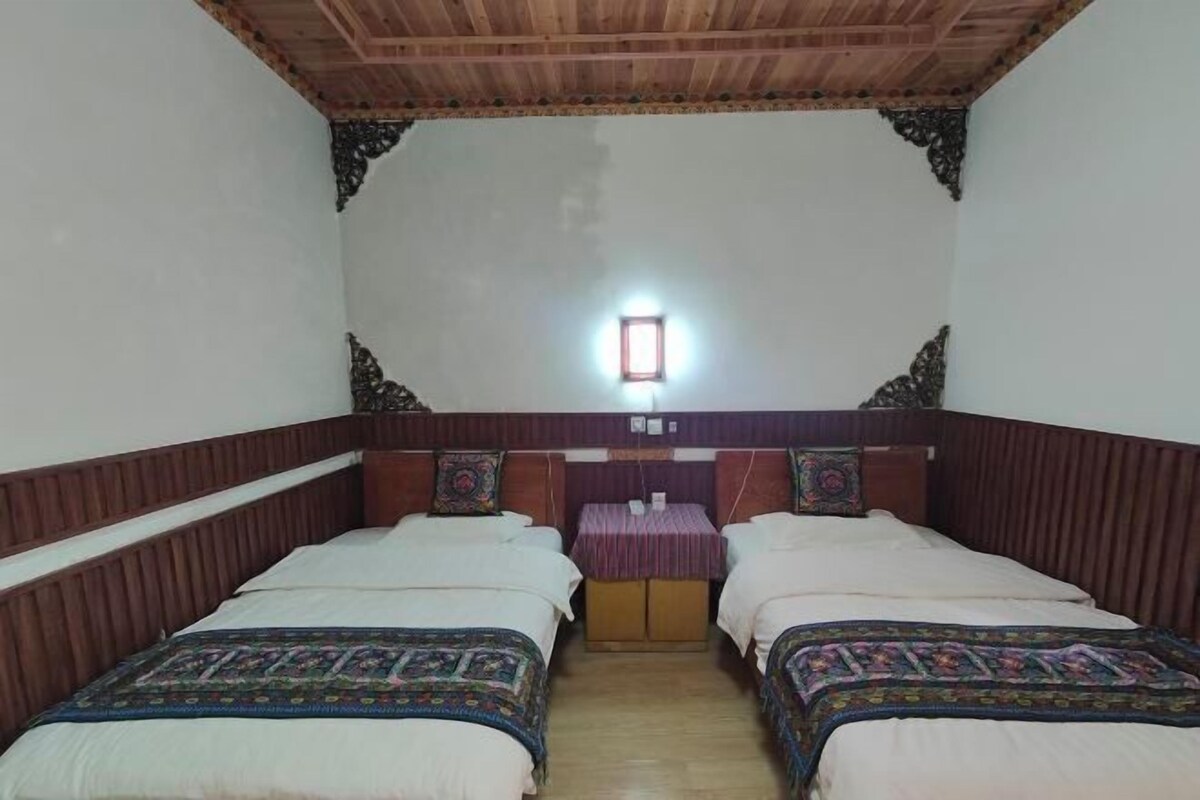 Habitación con dos camas, techo de madera y una mesita con una lámpara roja.