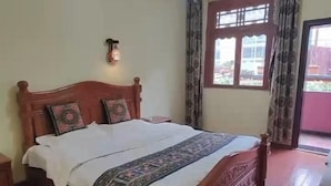 Ein Bett mit Holzbettgestell und gemustertem Bettbezug, ein Nachttisch, eine wandmontierte Leuchte und ein Fenster mit Vorhängen.