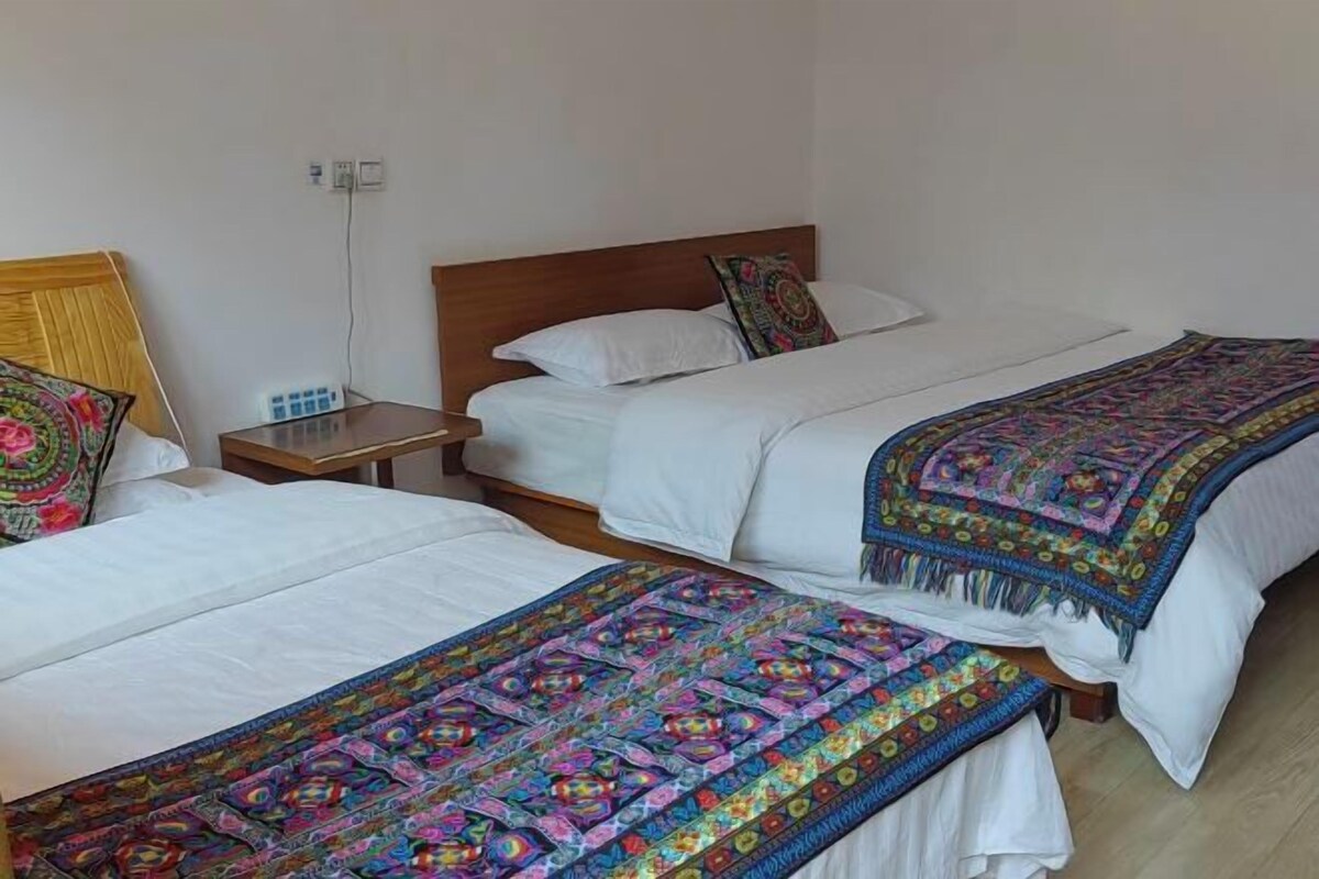 Habitación de hotel con dos camas, cada una con cabecera de madera, ropa de cama blanca y una manta de colores en una de ellas.