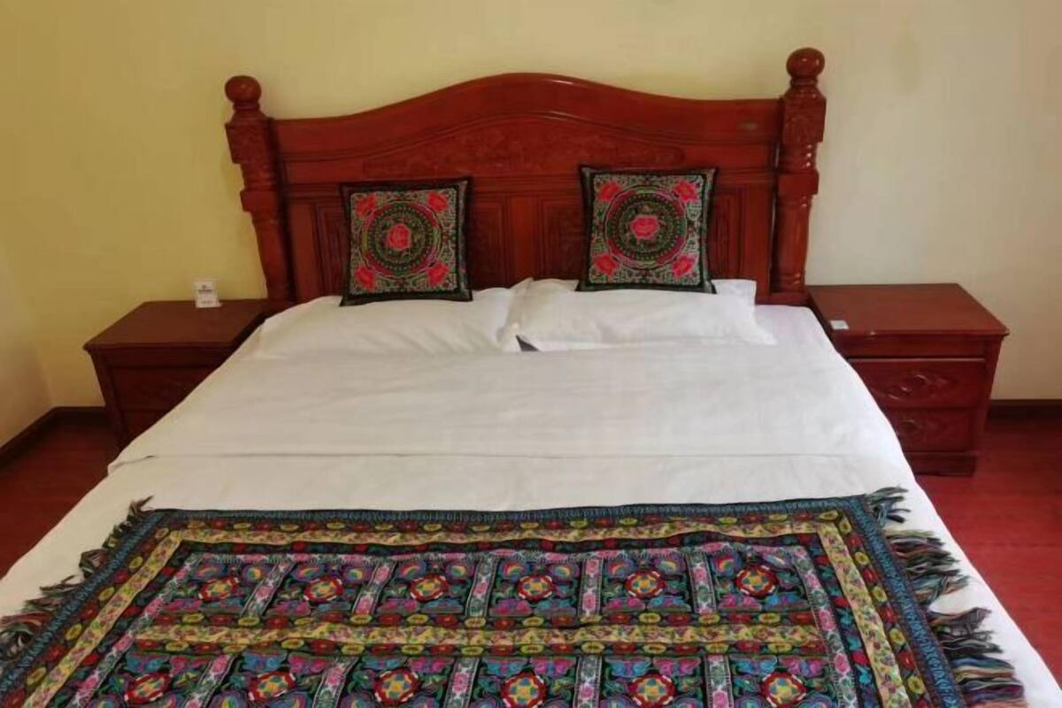 Un lit avec une tête de lit en bois, deux coussins décoratifs, un couvre-lit blanc et une couverture colorée.