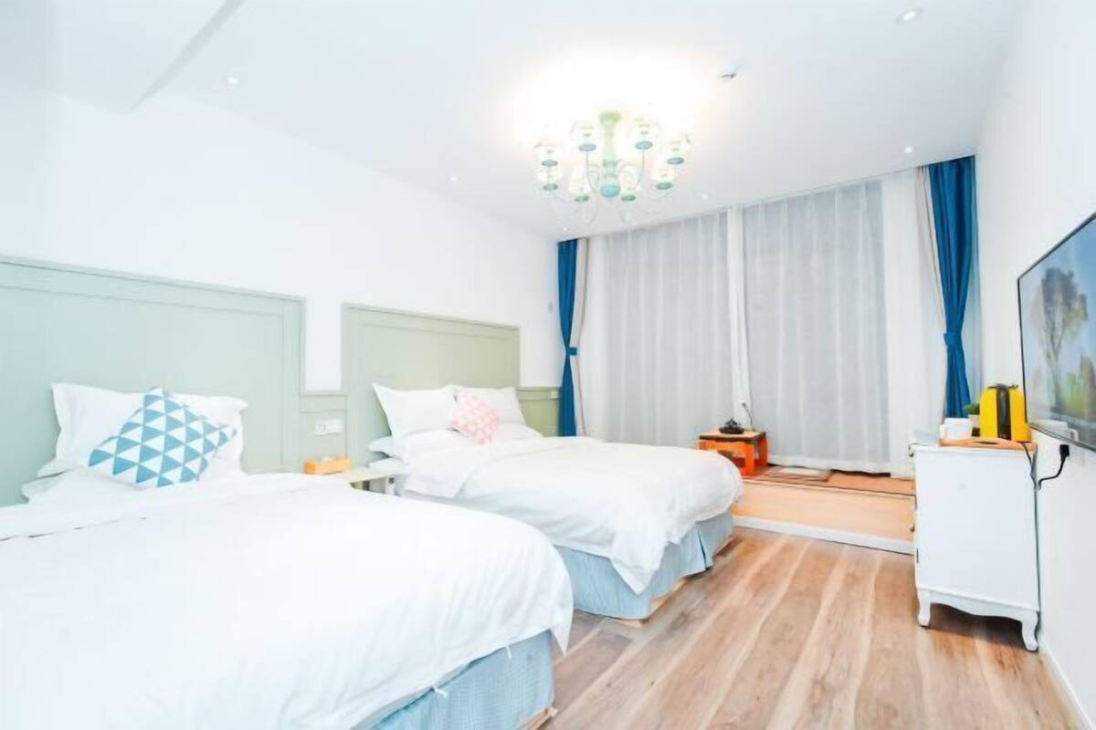 Una habitació d'hotel amb dos llits, una làmpada de cristall, un televisor i un terra de fusta.