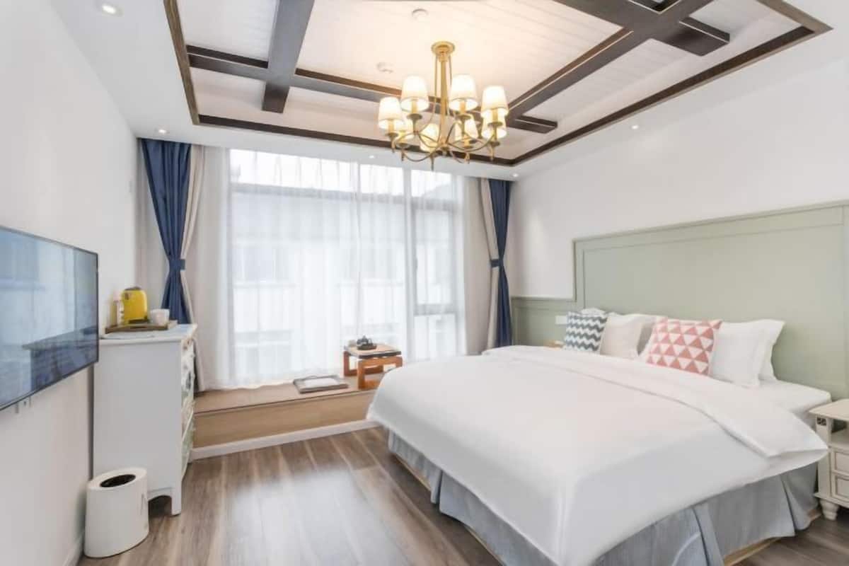 Habitació d'hotel amb un llit, televisió, escriptori i finestra amb cortines.