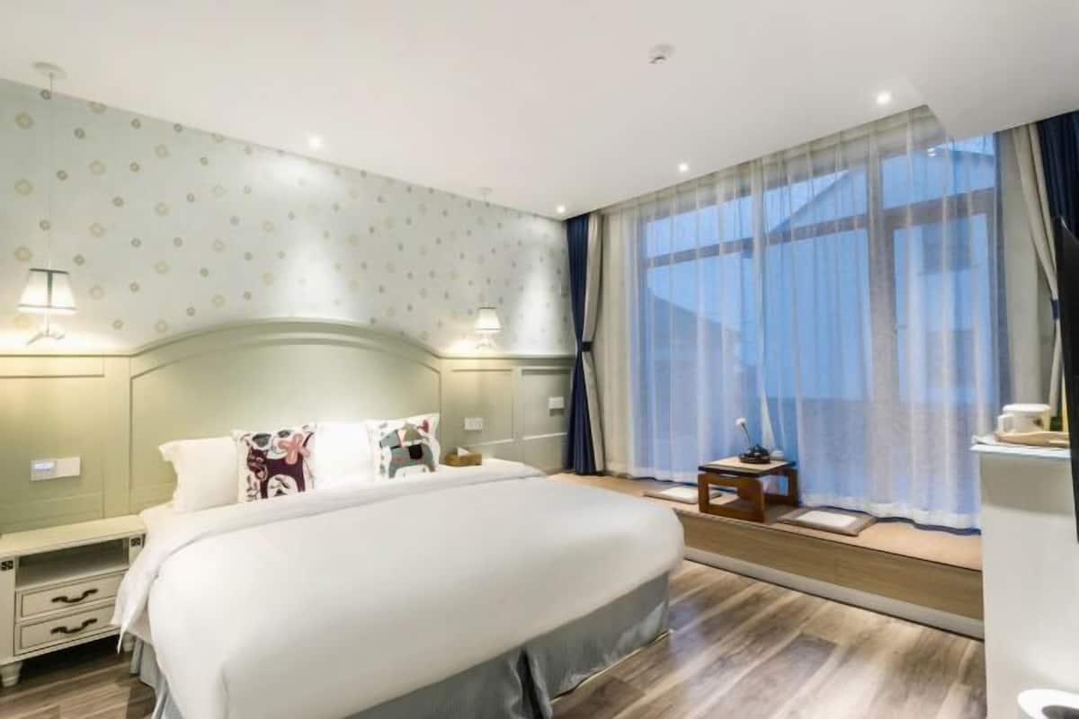 Una habitació d'hotel amb un llit gran, taules de nit, una finestra amb cortines i un terra de fusta.