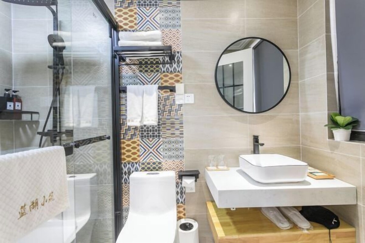 A modern bathroom with a glass shower enclosure, a white sink with a mirror above it, patterned tiles on the walls, and a small potted plant on the countertop.