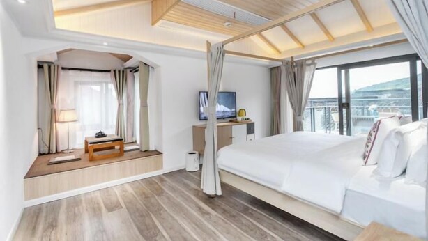 A modern hotel room with a large bed, a television, a desk, and a balcony with a view. - Lanhu Xiaozhu Hostel (Suzhou)