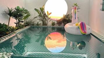 Une piscine intérieure bordée de carreaux, entourée de différentes plantes et agrémentée d’un flamant rose décoratif.