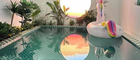 Una piscina interna con bordo piastrellato, circondata da diverse piante e un fenicottero decorativo.