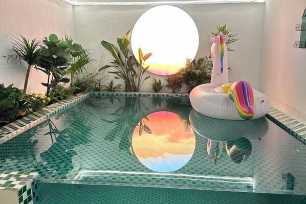 An indoor swimming pool with a tiled edge, surrounded by various plants and a decorative flamingo. - Lanhu Xiaozhu Hostel (Suzhou)