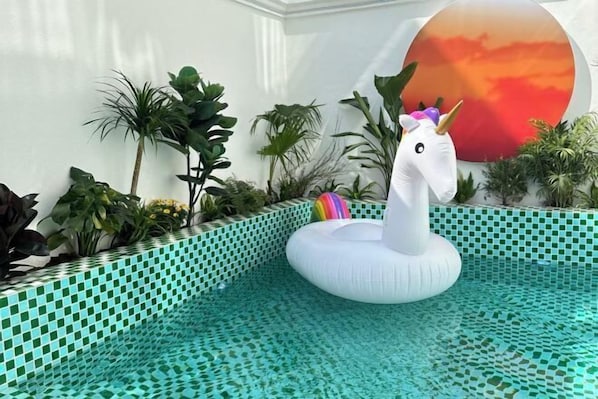 A pool area with a decorative unicorn float, surrounded by various plants and a tiled edge. - Lanhu Xiaozhu Hostel (Suzhou)