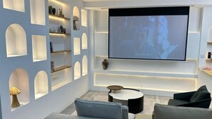 A modern living room with a flat-screen TV mounted on the wall, a sofa, a coffee table, and built-in shelving with decorative items. - Lanhu Xiaozhu Hostel (Suzhou)