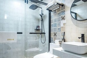 Un bagno moderno con cabina doccia in vetro, un lavandino bianco e una parete rivestita di piastrelle con motivo geometrico.