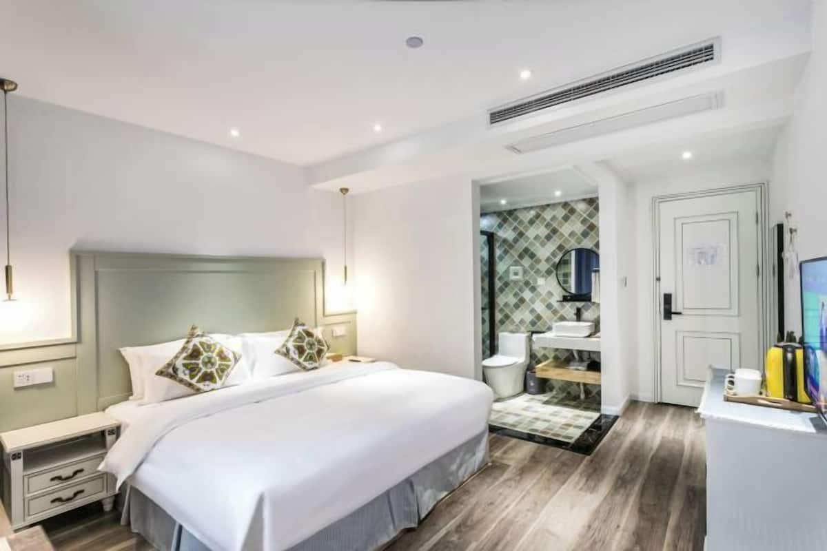 Habitació d'hotel moderna amb un llit gran, taules de nit, un armari encastrat, un bany amb dutxa i una televisió.