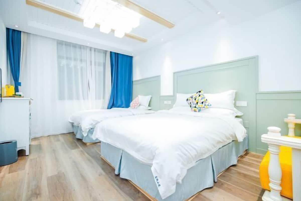 Habitació d'hotel amb dos llits, una taula de treball i una finestra amb cortines blaves.