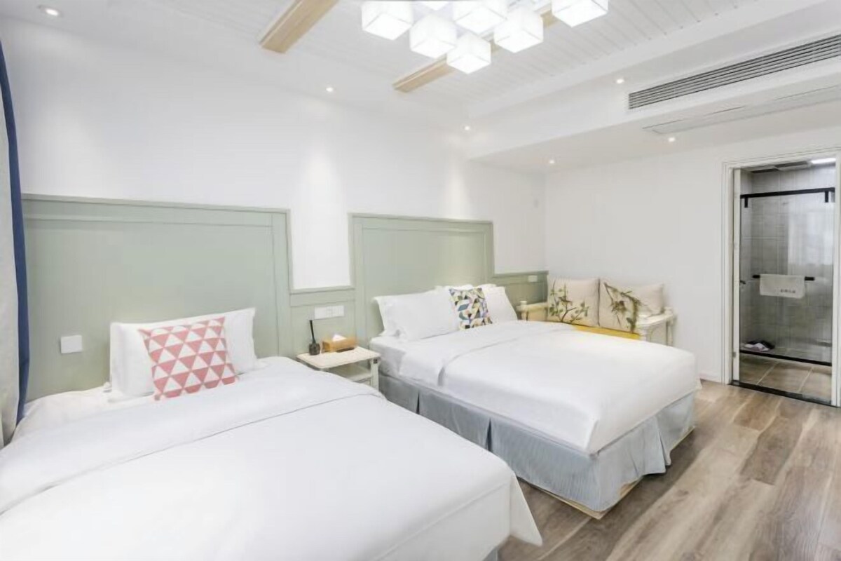 A hotel room with two beds, a small bedside table with a lamp, and a large window.