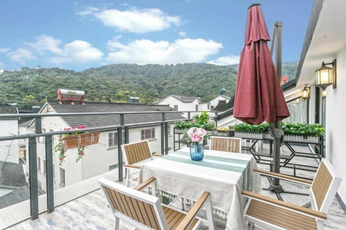 A balcony with a table, chairs, a vase with flowers, and a red umbrella.