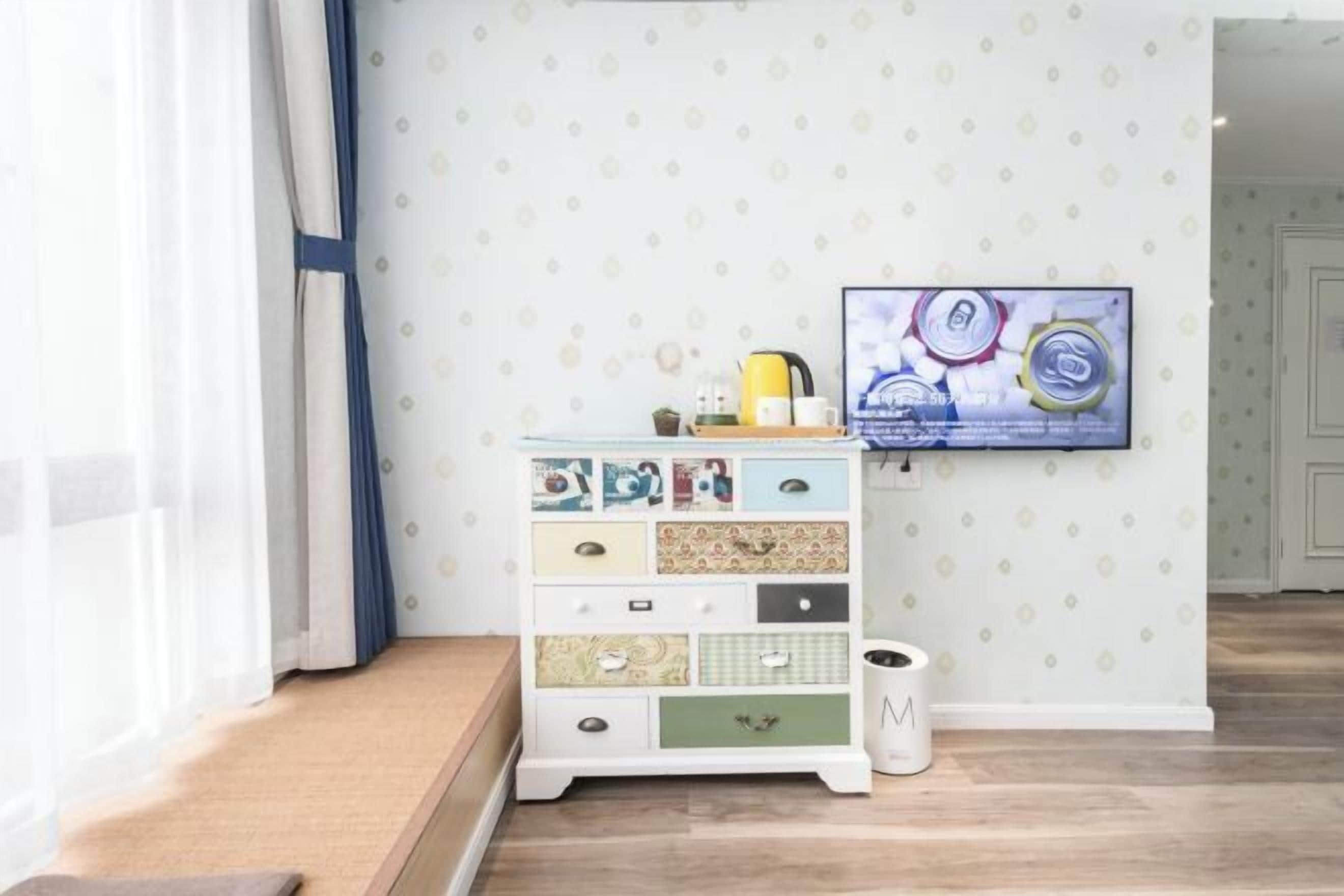 Una habitación con un armario blanco con varios cajones, un televisor en la pared y un papel tapiz estampado.