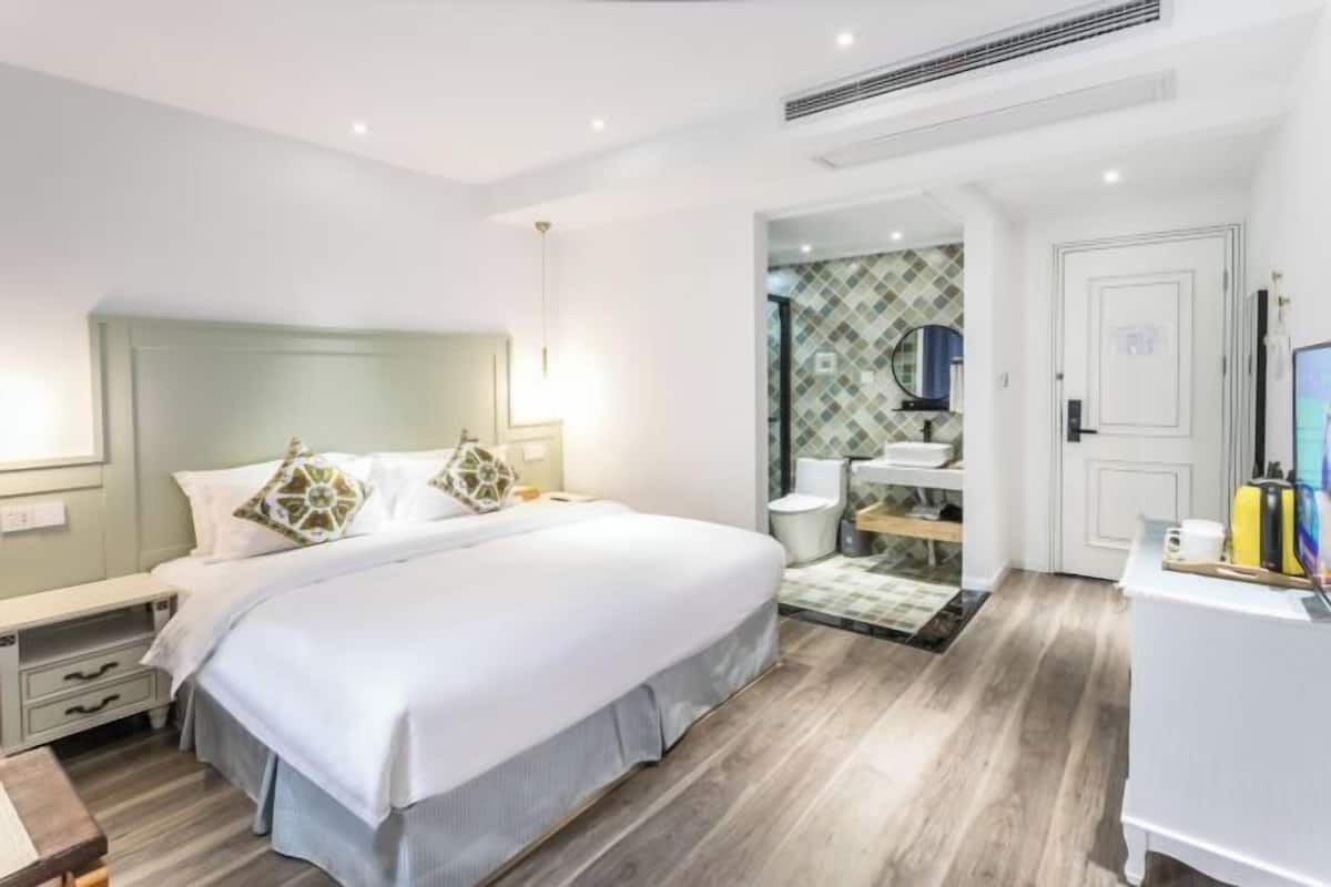 Habitació d'hotel moderna amb un llit gran, taules de nit, un escriptori i un bany visible a través d'una porta oberta.