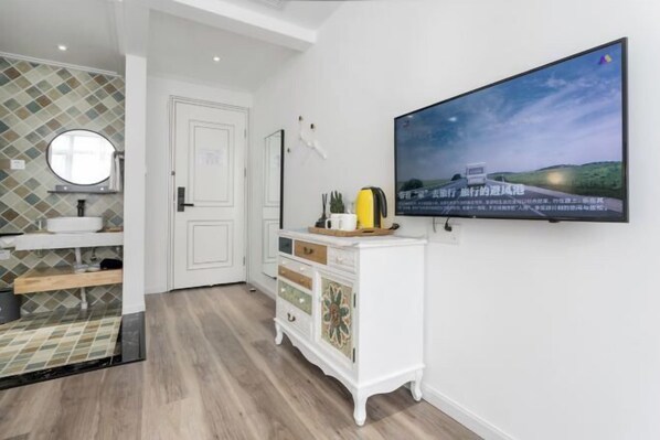A modern bathroom with a tiled backsplash, a round mirror, a white vanity, a television mounted on the wall, and a wooden floor. - Lanhu Xiaozhu Hostel (Suzhou)