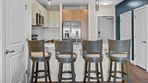 A modern kitchen with three bar stools, a stainless steel refrigerator, and a microwave. - Beverly Hills Penthouse Suite (Nashville)