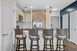 A modern kitchen with three bar stools, a stainless steel refrigerator, and a microwave.